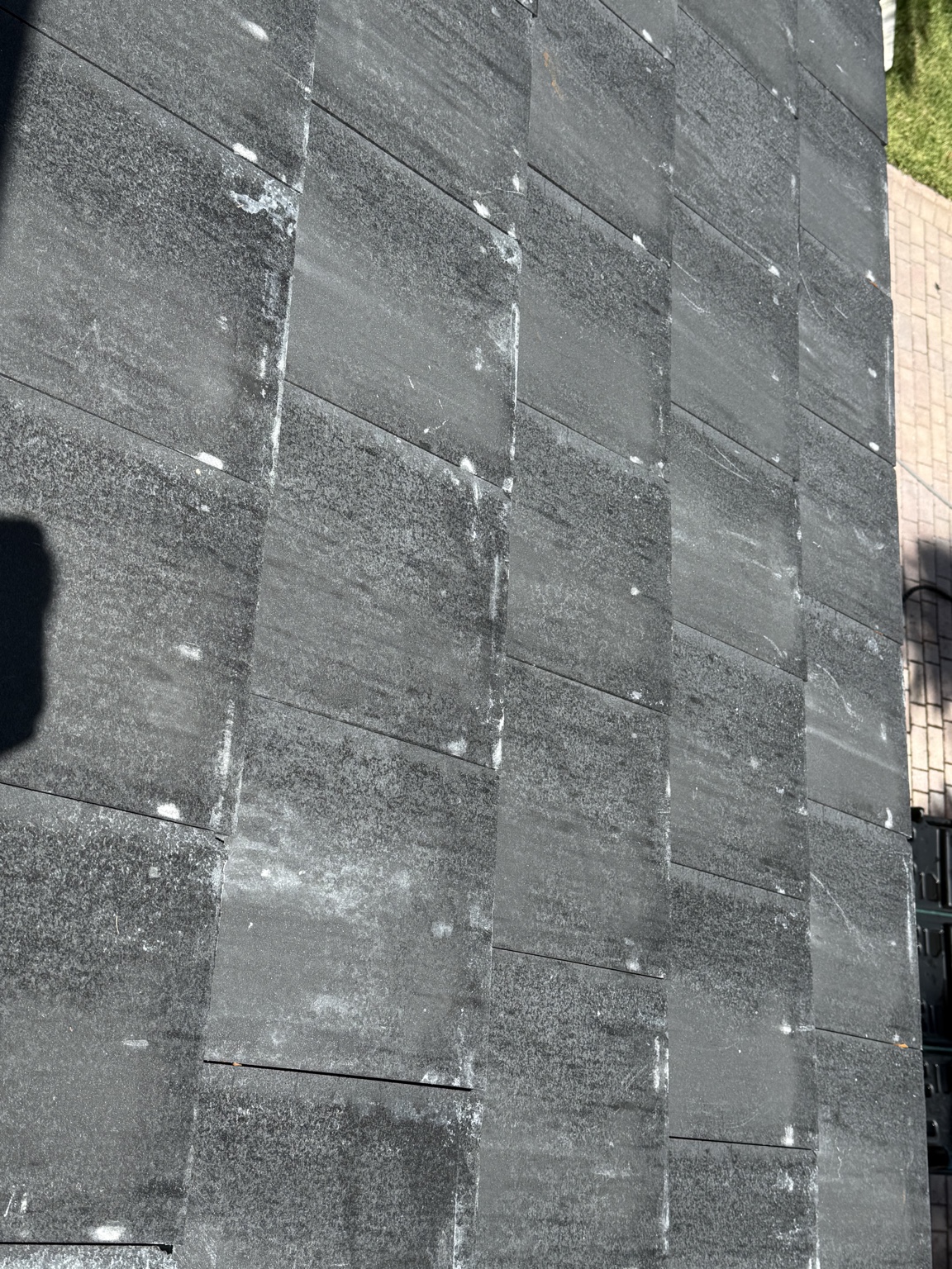 Rows of dark concrete roof tiles showing repeated pale edge marks and broad gray areas