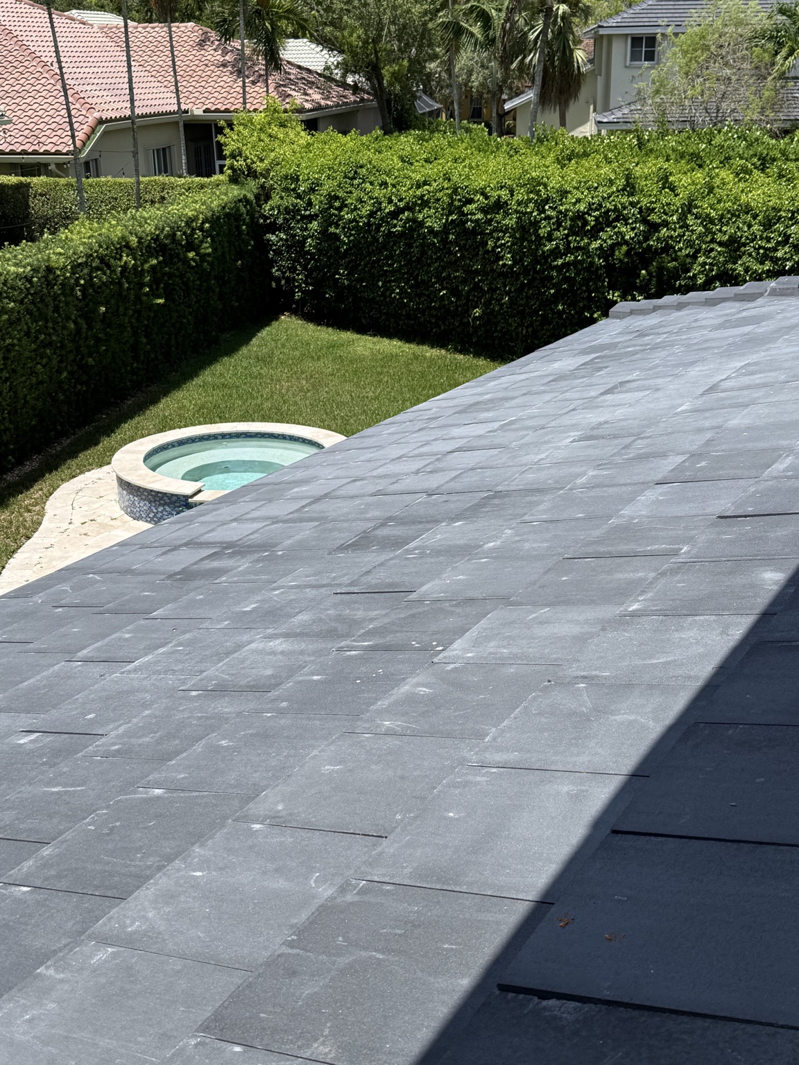 Wide view of a dark gray tile roof with widespread lighter streaks and marks